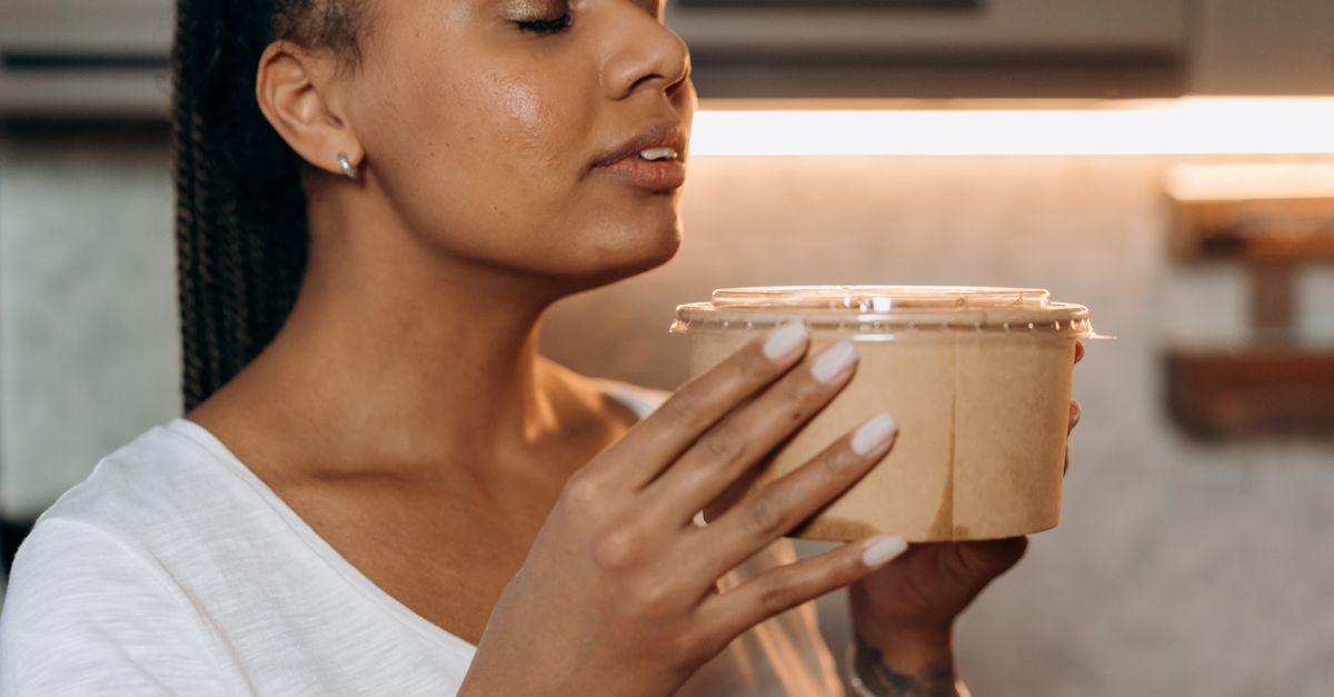 A woman savoring the aroma of a takeaway meal in a cozy kitchen setting.